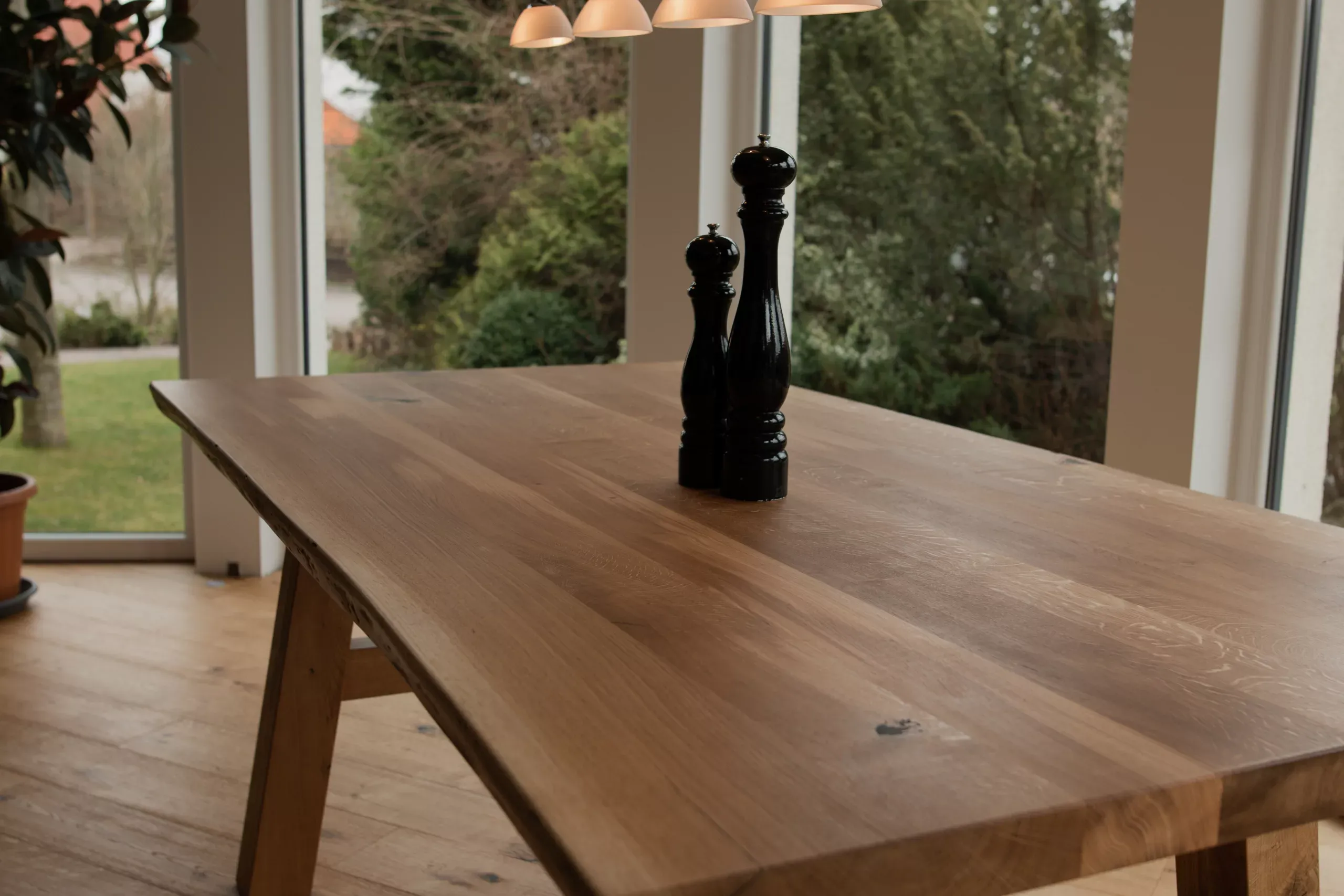 Massivholz-Esstisch mit zwei Pfeffermühlen vor Gartenfenster